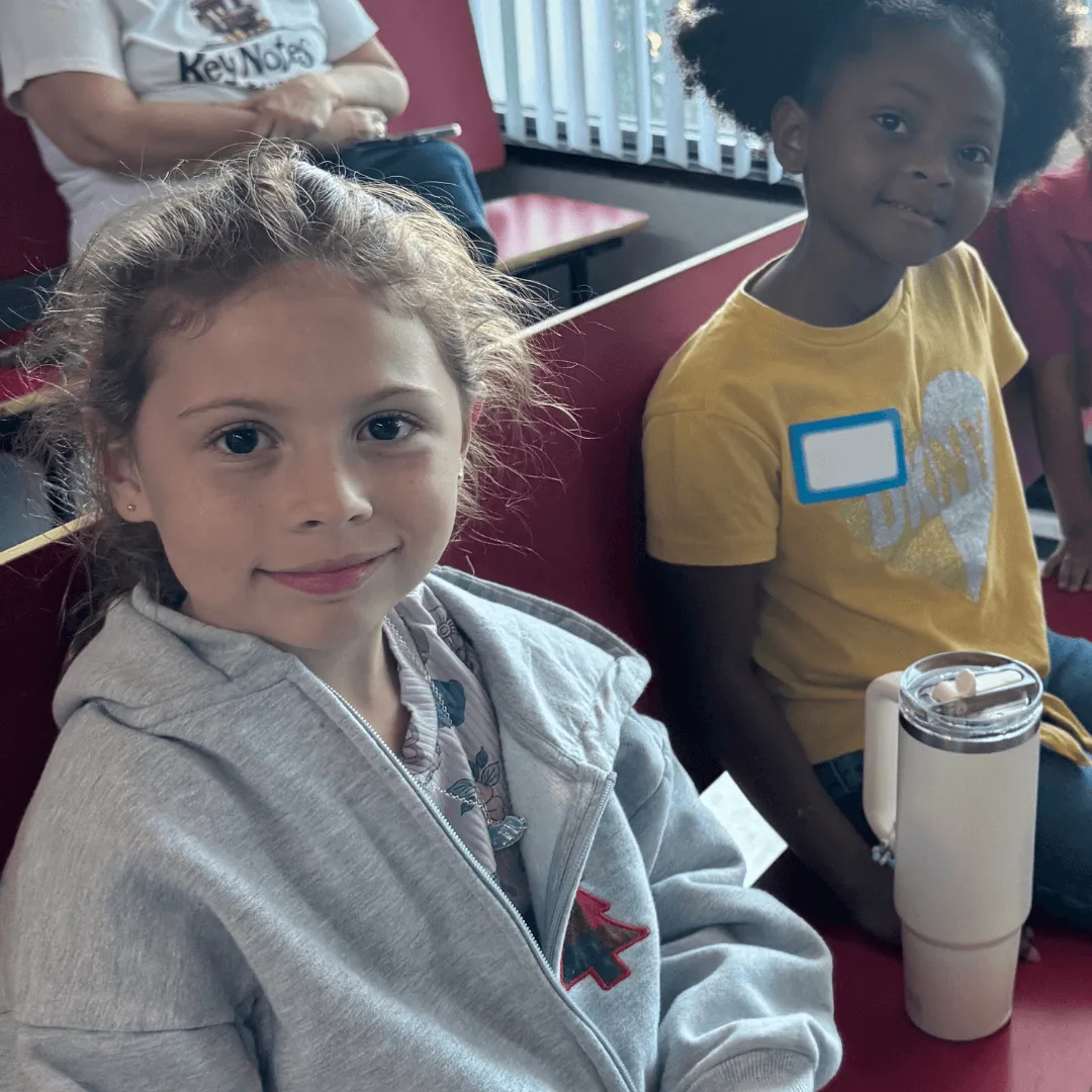 Two young girls sitting together at a Key Chorale education program, smiling as they participate in a community music activity.